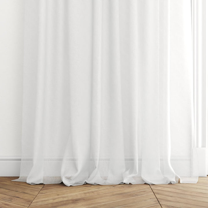 The hem of Whisper ecru semi-transparent curtains gracefully cascading onto a herringbone timber floor.